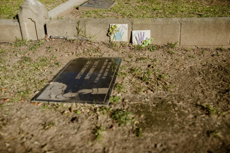 A gravesite with a memorial plaque and children's art in a cemetery setting.
