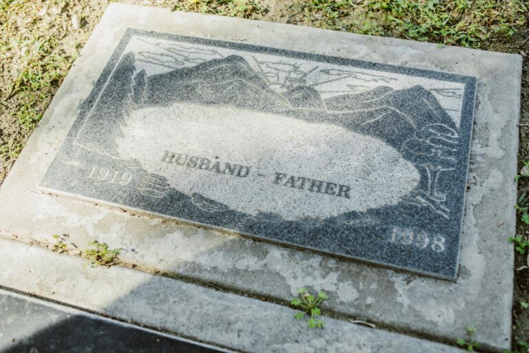 Close-up of a weathered granite tombstone with engraving of 'Husband' and 'Father' including dates 1919-1998.