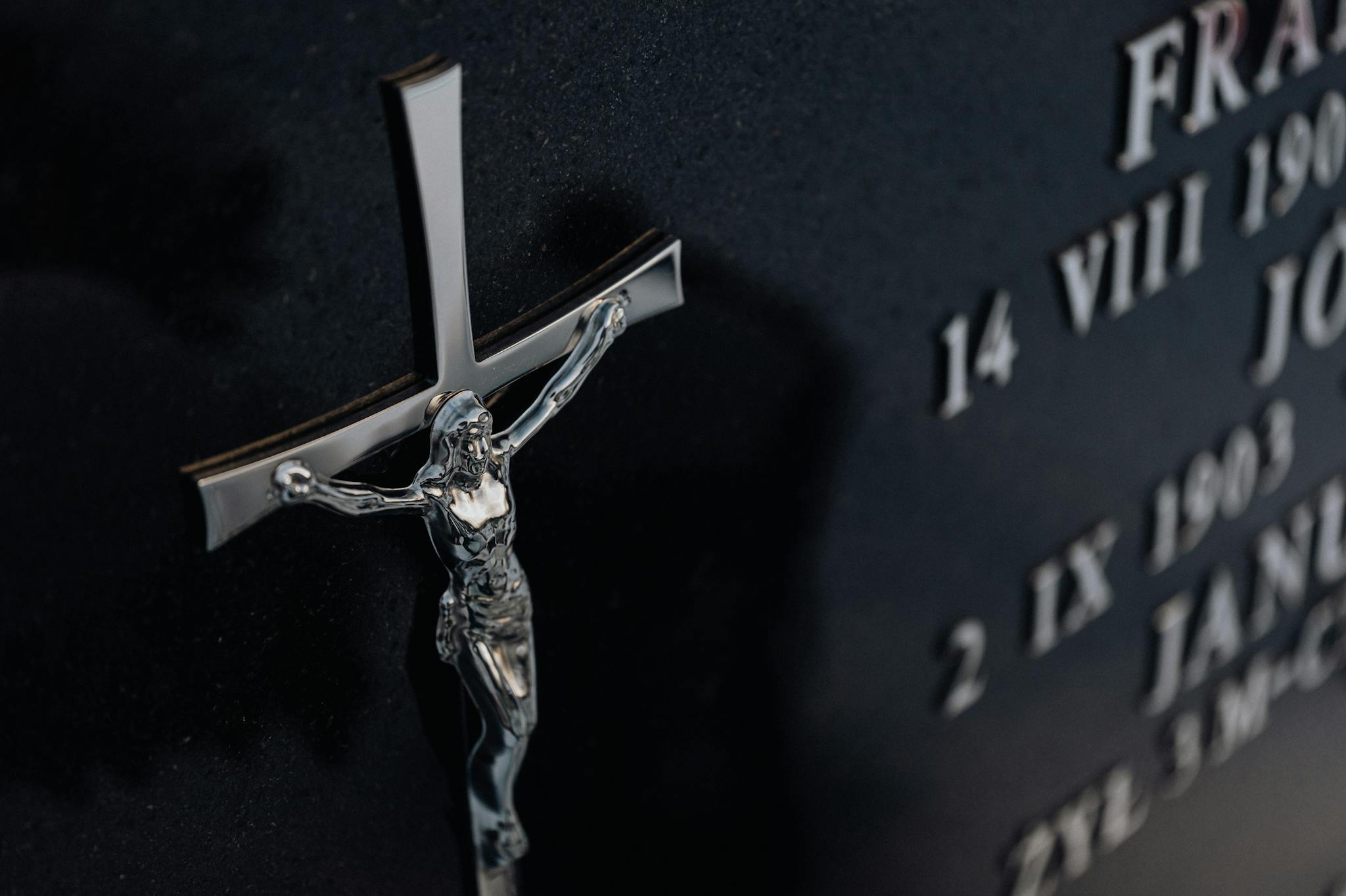 Detailed photo of a cross on a tombstone featuring engraved text, representing religious themes.